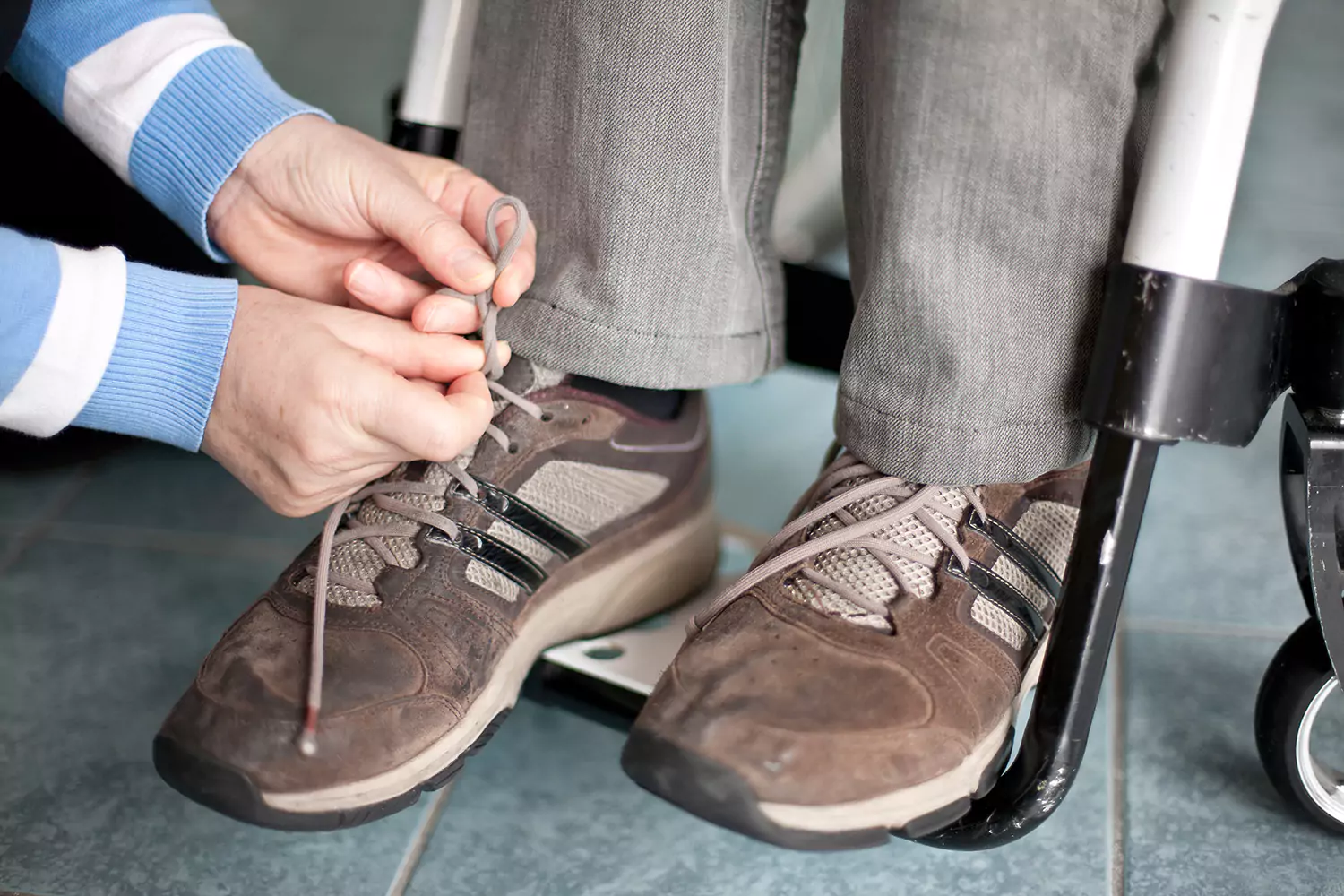A woman is helping a man in a wheelchair with tying up his shoe laces