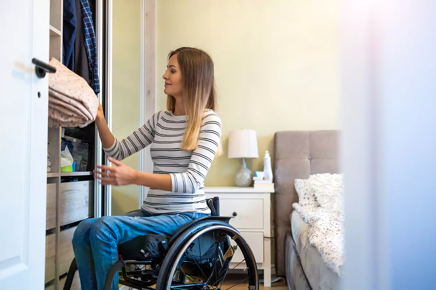 A woman in a wheelchair in putting away folder laundry in her bedroom