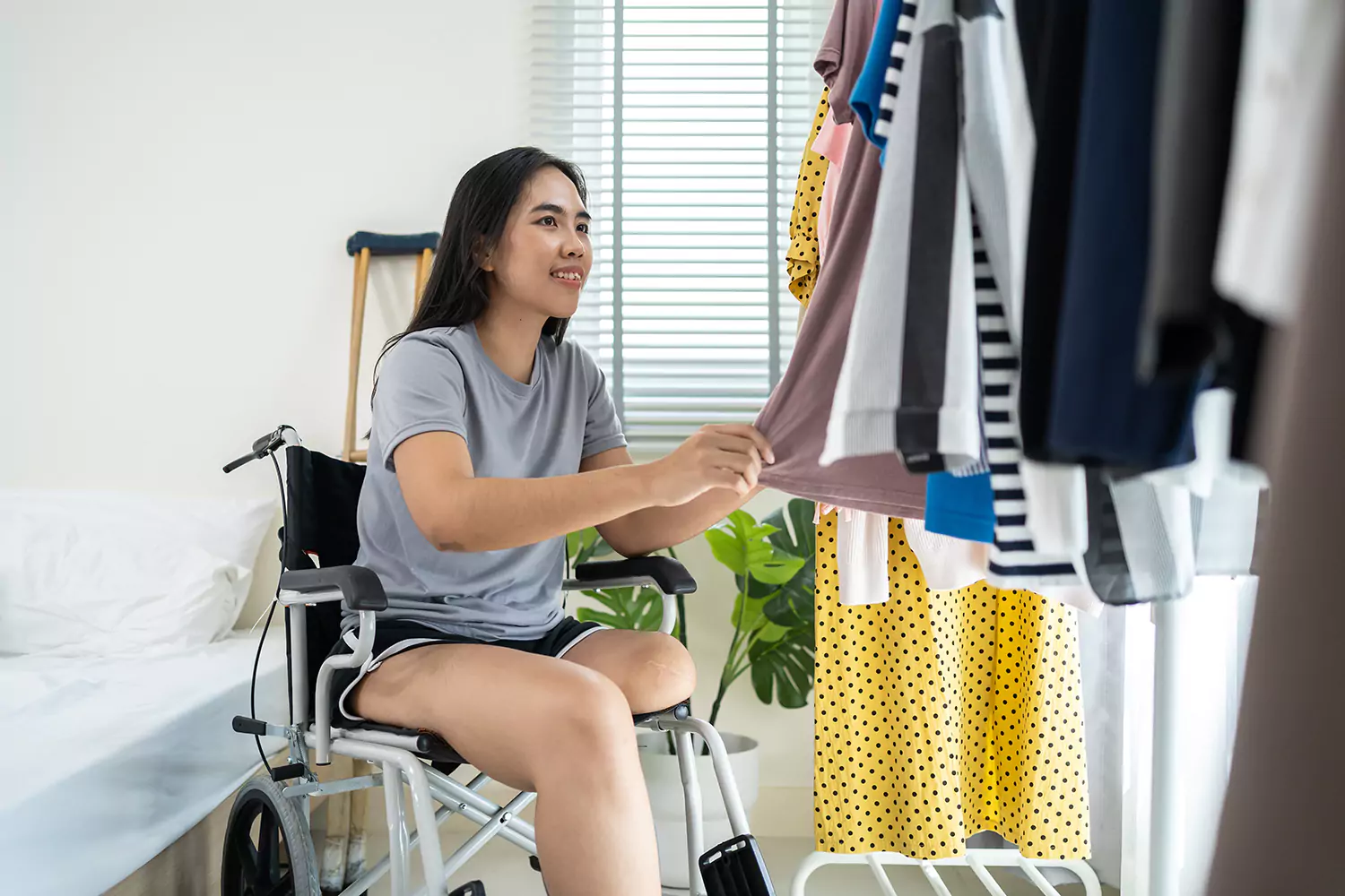 A young woman with an amputated leg is selecting clothes to wear in her room